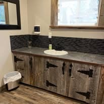Bathroom vanity with reclaimed wood cabinets, dark stone backsplash, and vessel sink