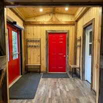 Second angle of the red door entry with vaulted wood ceiling and coat hooks